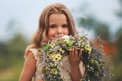 Photo of Cute little girl holding wreath made of beautiful flowers outdoors