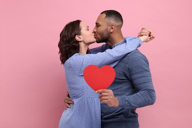 Photo of Lovely couple with red paper heart kissing on pink background. Valentine's day celebration