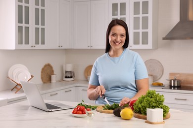 Photo of Beautiful overweight woman preparing healthy meal at table in kitchen
