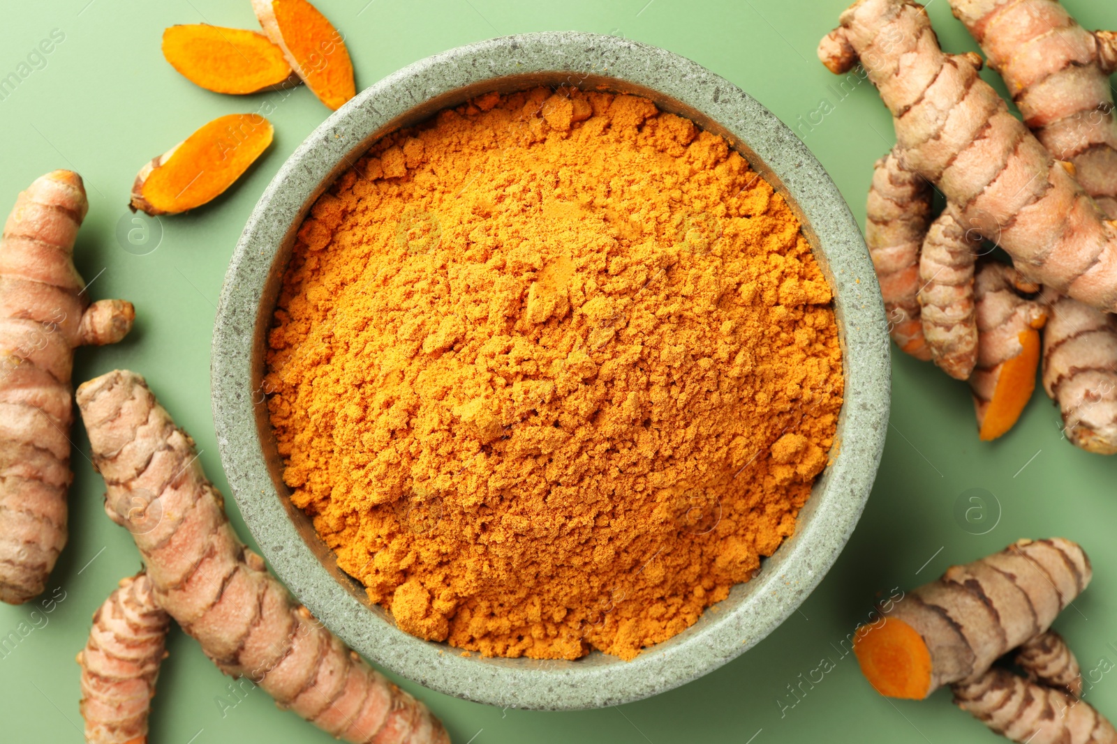 Photo of Aromatic turmeric powder and raw roots on green background, flat lay