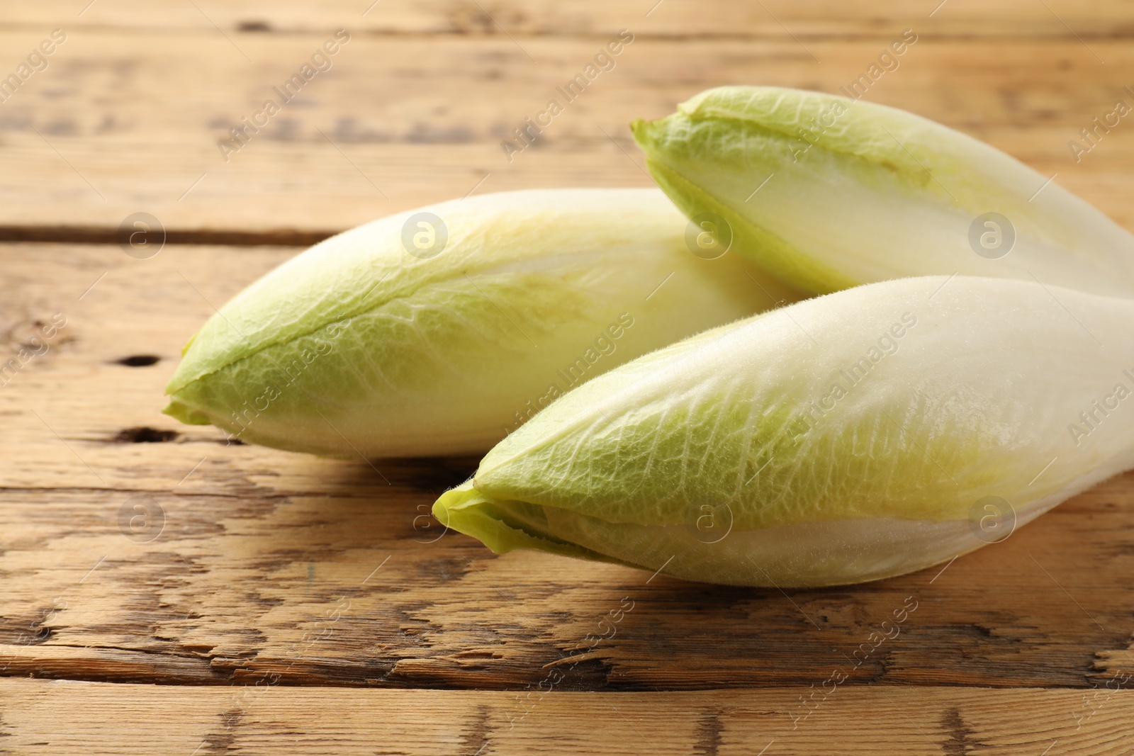 Photo of Fresh raw Belgian endives (chicory) on wooden table, closeup