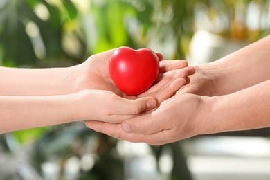 Young and elderly women holding red heart in hands on blurred green background, closeup