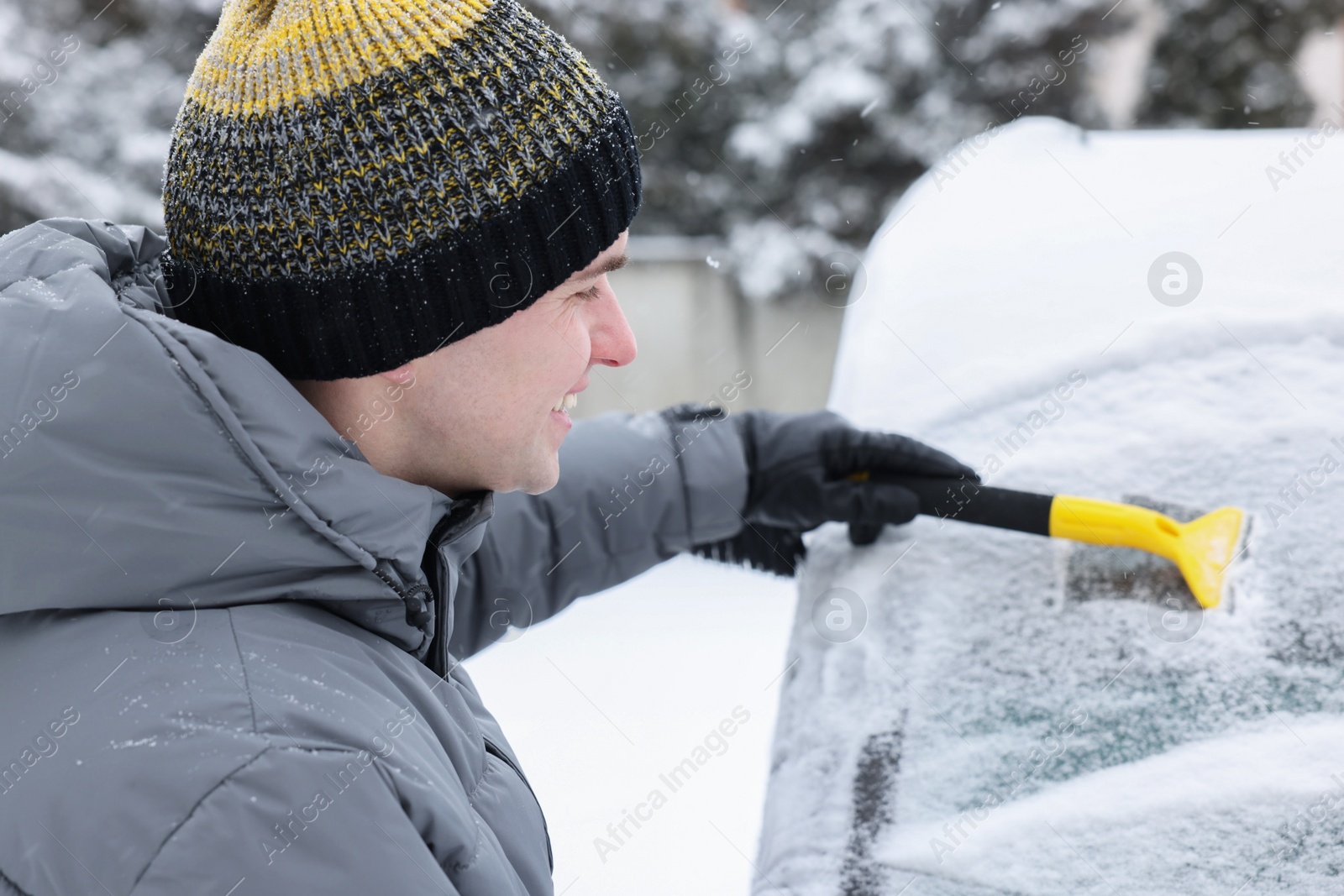 Photo of Man cleaning snow from car windshield outdoors