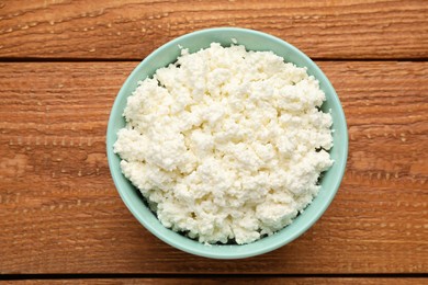 Photo of Delicious fresh cottage cheese in bowl on wooden table, top view