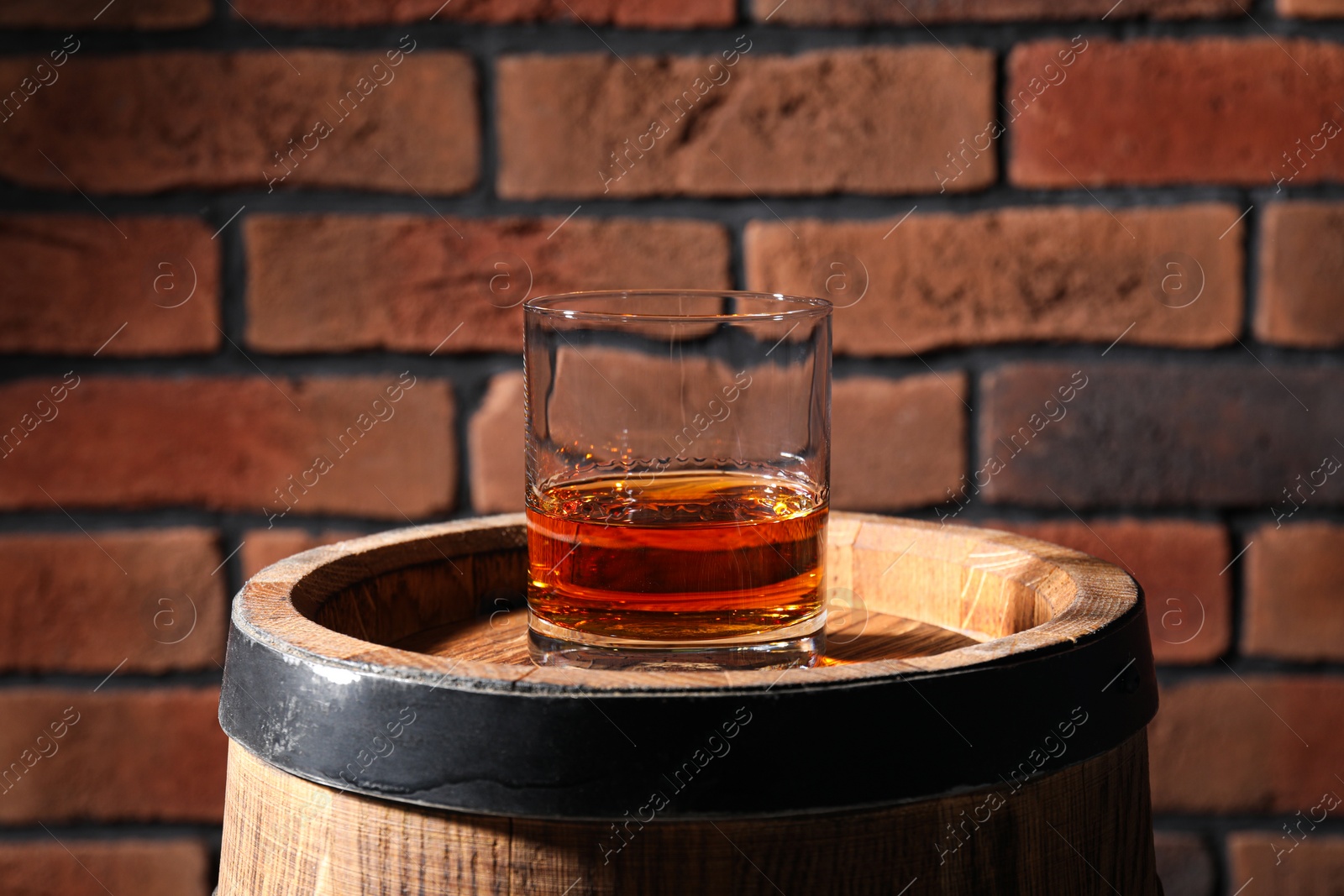 Photo of Glass of whiskey on wooden barrel against brick wall