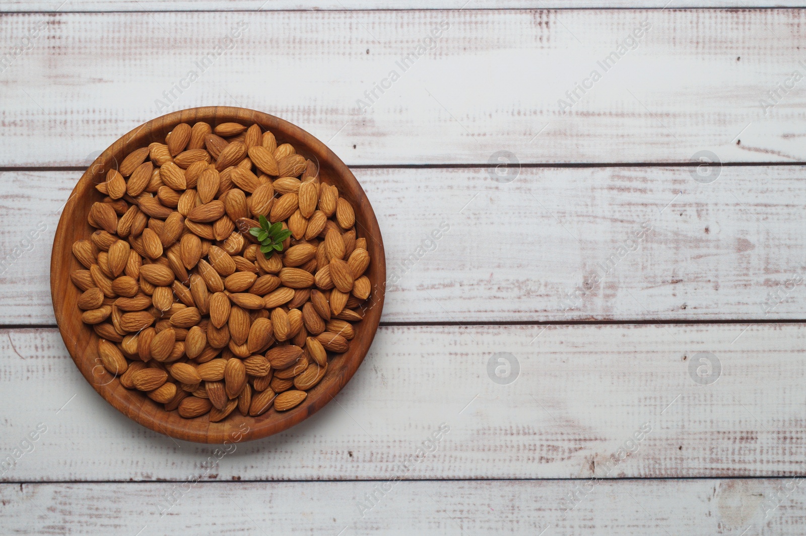 Photo of Plate with tasty almonds on white wooden table, top view. Space for text