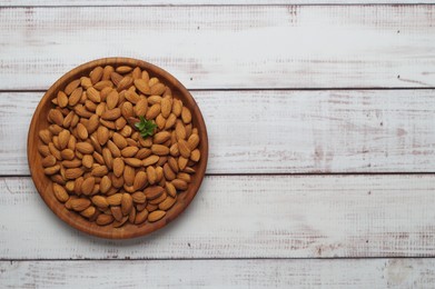 Plate with tasty almonds on white wooden table, top view. Space for text