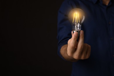 Photo of Glow up your ideas. Closeup view of man holding light bulb on black background, space for text