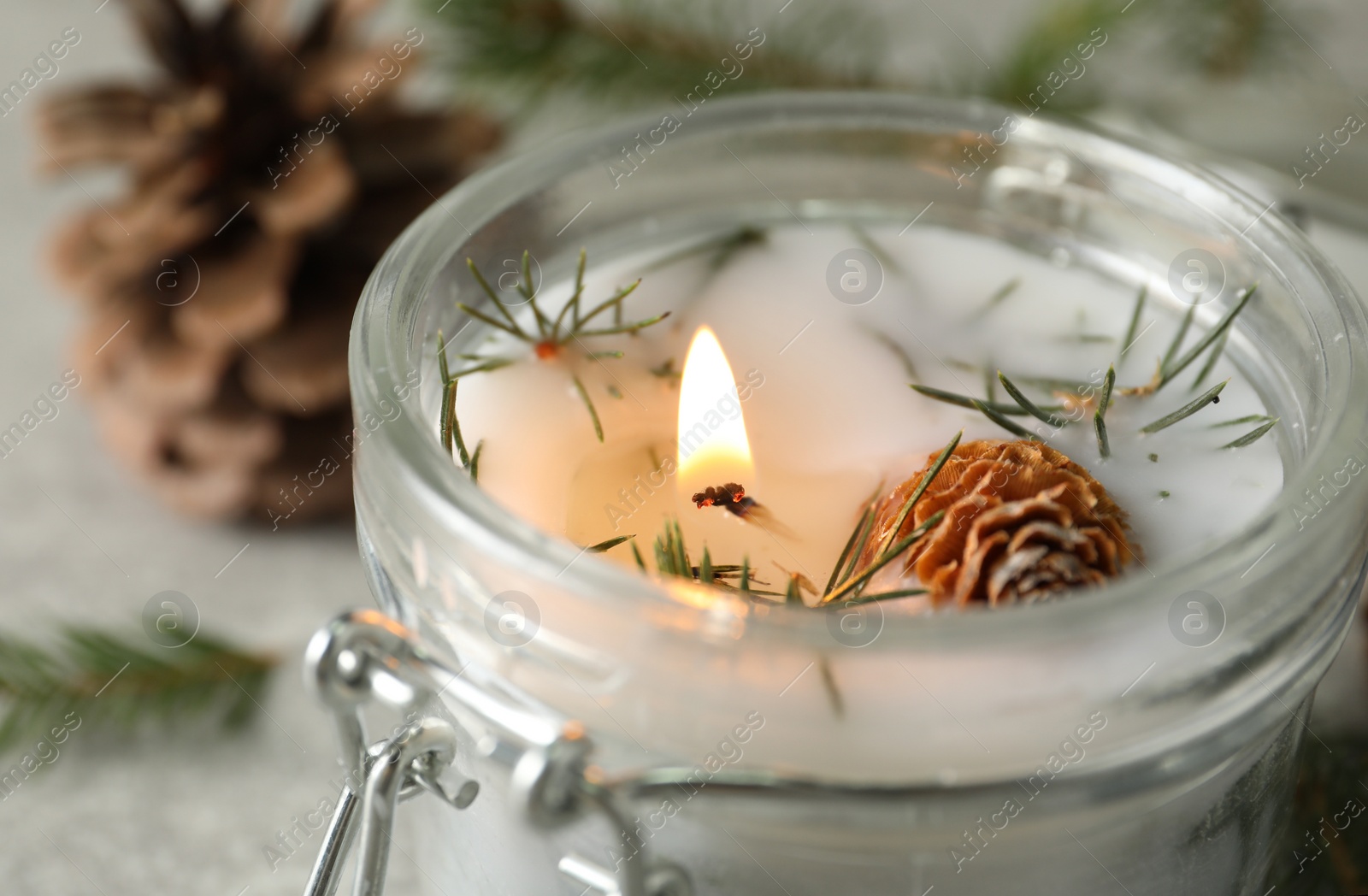 Photo of Burning scented conifer candle in glass jar, closeup view