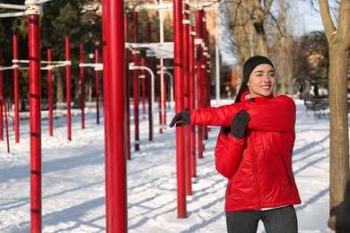 Happy woman doing sports exercises in snowy park on winter day