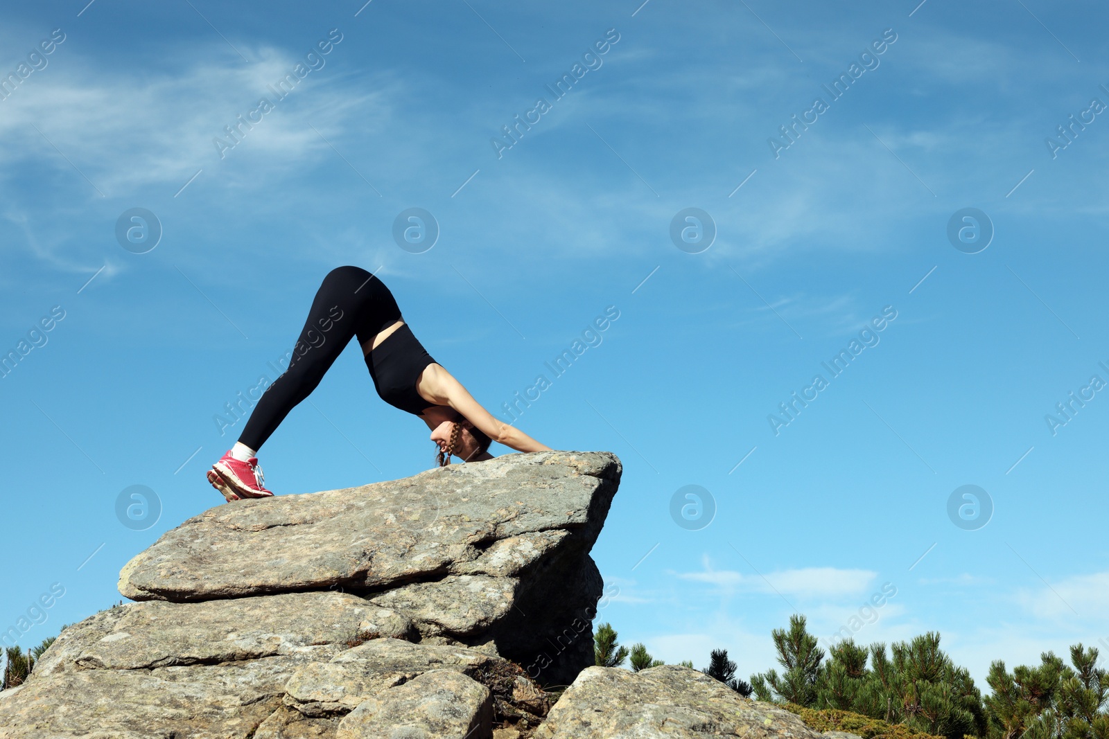 Photo of Beautiful young woman practicing yoga on rock in mountains