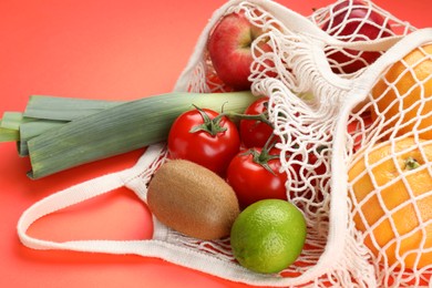 Photo of String bag with different vegetables and fruits on red background, closeup