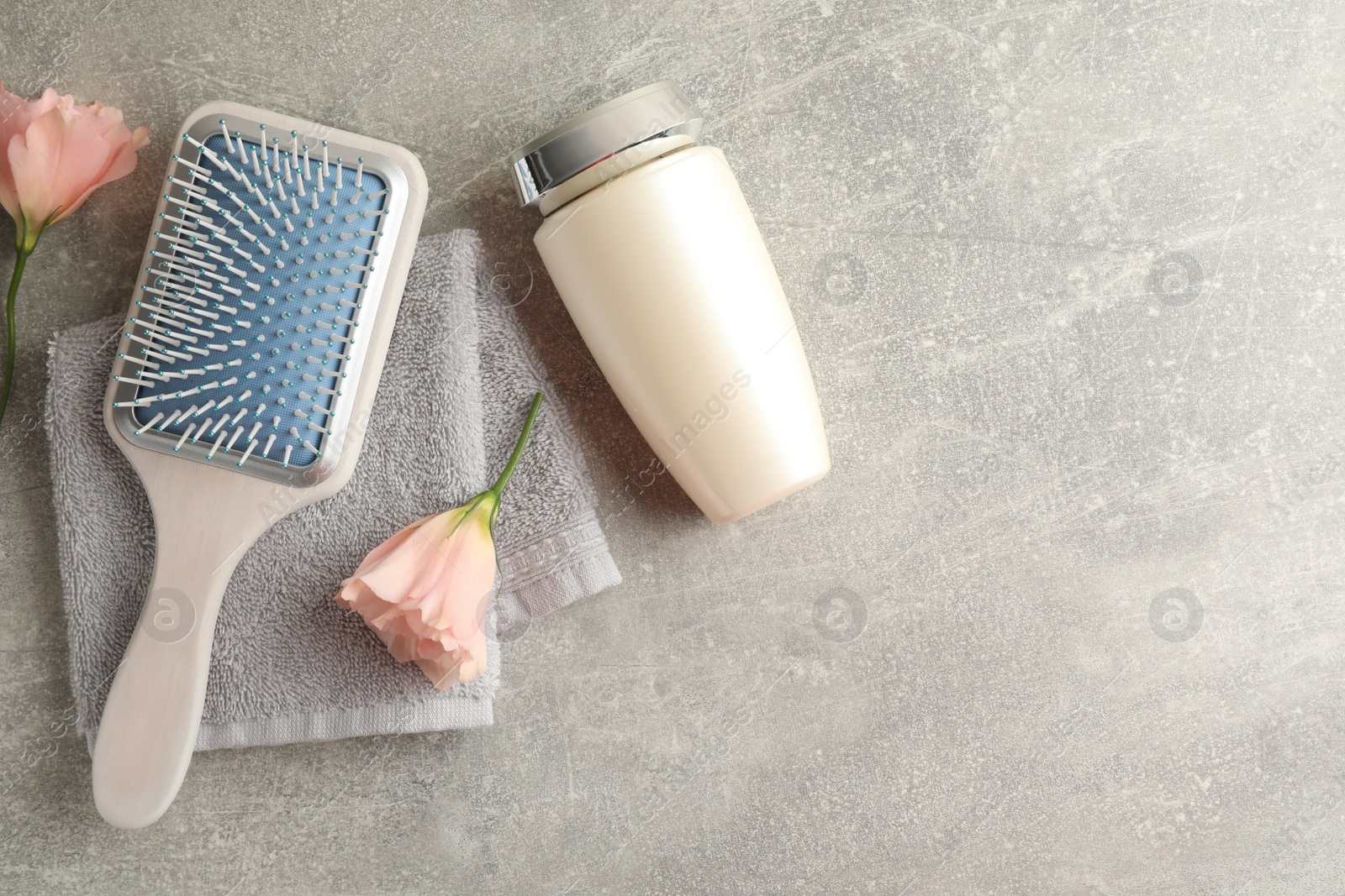 Photo of Bottle of hair care cosmetic product, brush and flowers on light grey table, flat lay. Space for text