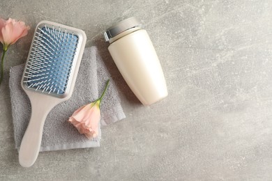 Photo of Bottle of hair care cosmetic product, brush and flowers on light grey table, flat lay. Space for text