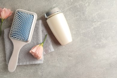 Bottle of hair care cosmetic product, brush and flowers on light grey table, flat lay. Space for text