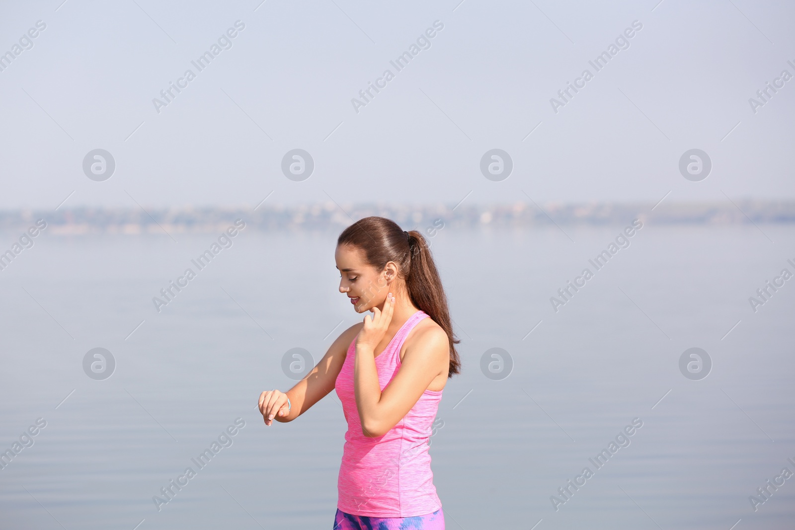 Photo of Young woman checking pulse outdoors on sunny day