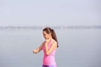 Photo of Young woman checking pulse outdoors on sunny day