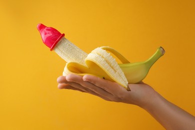 Photo of Woman holding banana in condom on orange background, closeup. Safe sex concept