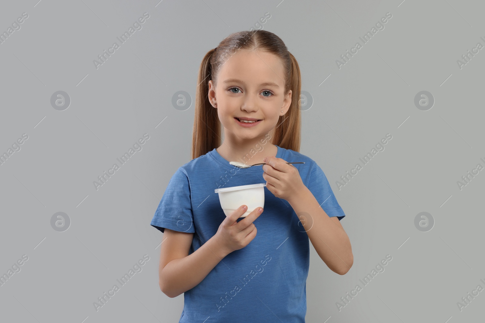 Photo of Cute little girl with tasty yogurt on gray background