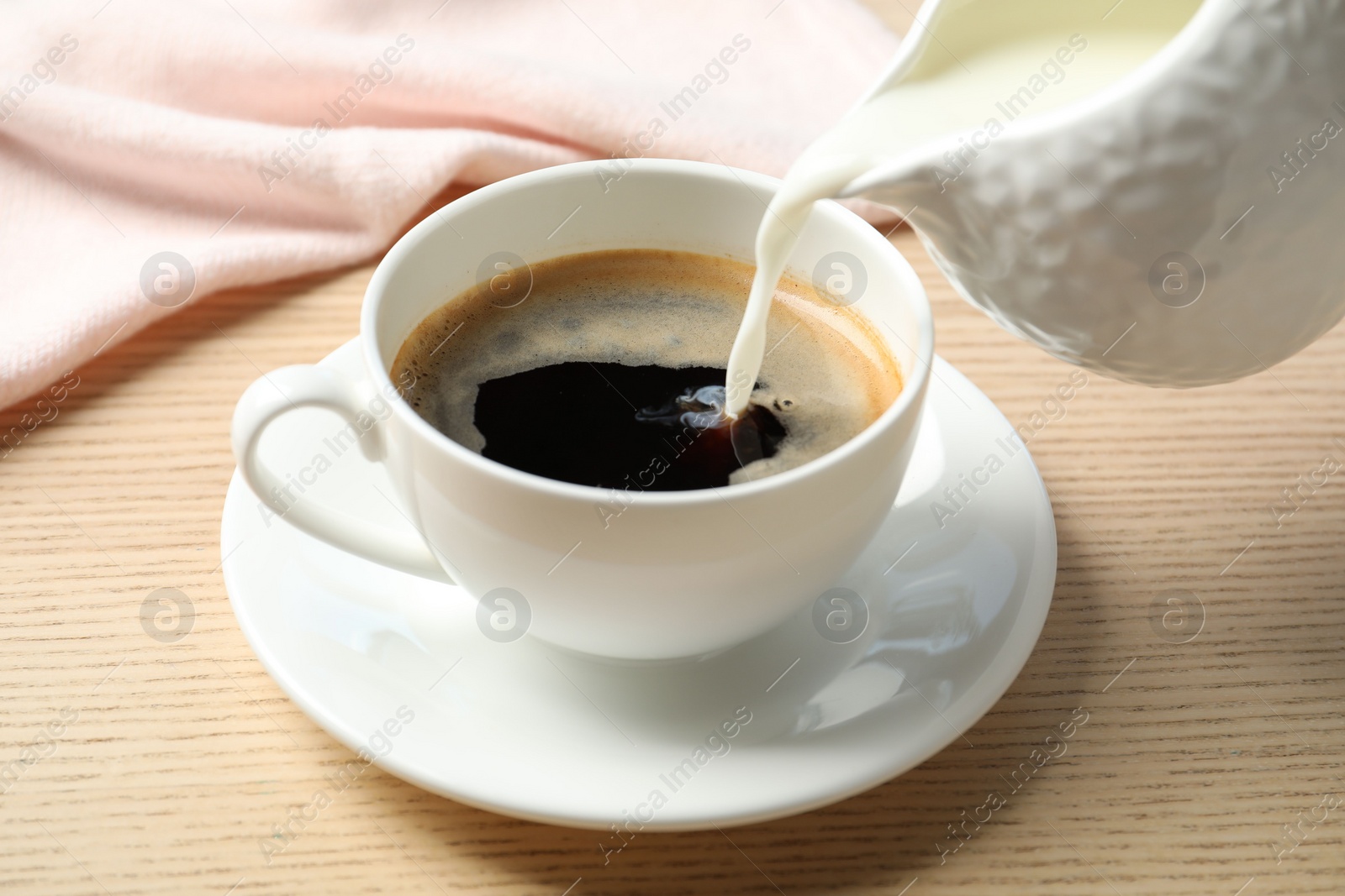 Photo of Pouring milk into cup of hot coffee on wooden table