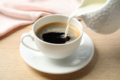 Pouring milk into cup of hot coffee on wooden table