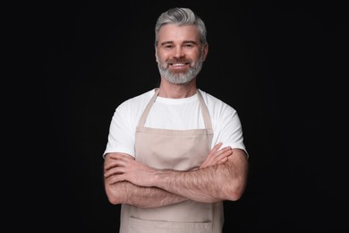 Photo of Happy man wearing kitchen apron on black background. Mockup for design