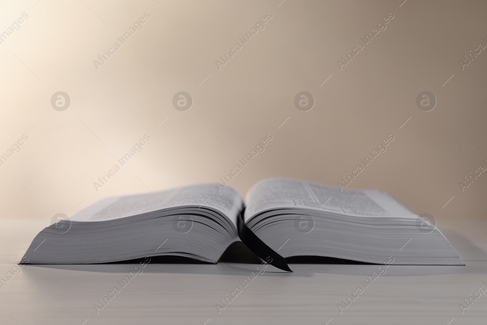 Photo of Open Bible on white wooden table against beige background. Space for text