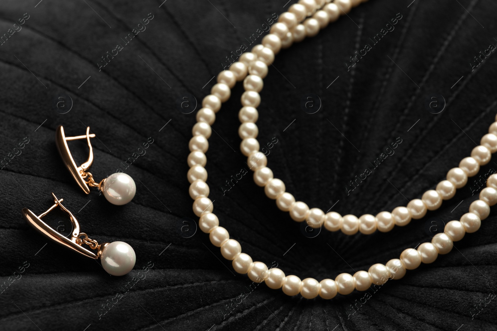 Photo of Elegant necklace and golden earrings with pearls on black fabric, closeup