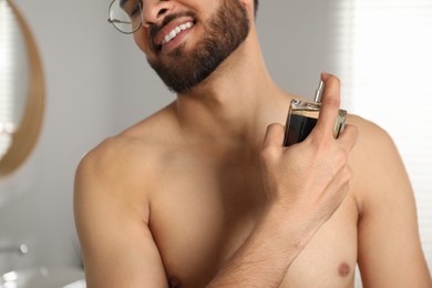 Young man spraying luxury perfume indoors, closeup