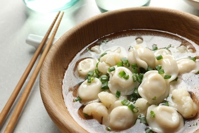 Plate of tasty dumplings with green onion in broth on grey table, closeup