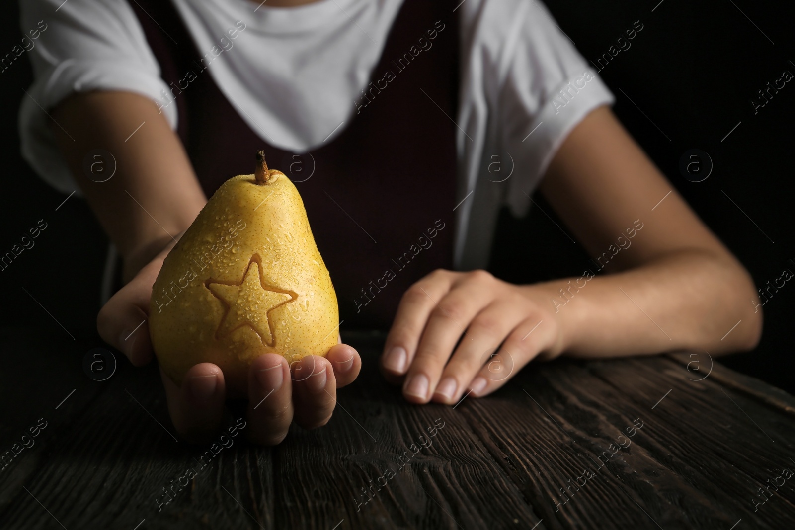 Photo of Woman holding ripe pear with star at table against dark background. Fruit carving