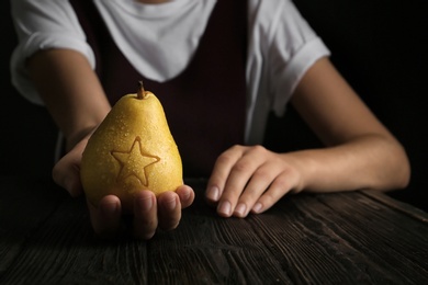 Woman holding ripe pear with star at table against dark background. Fruit carving