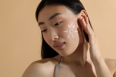 Beautiful young woman with sun protection cream on her face against beige background