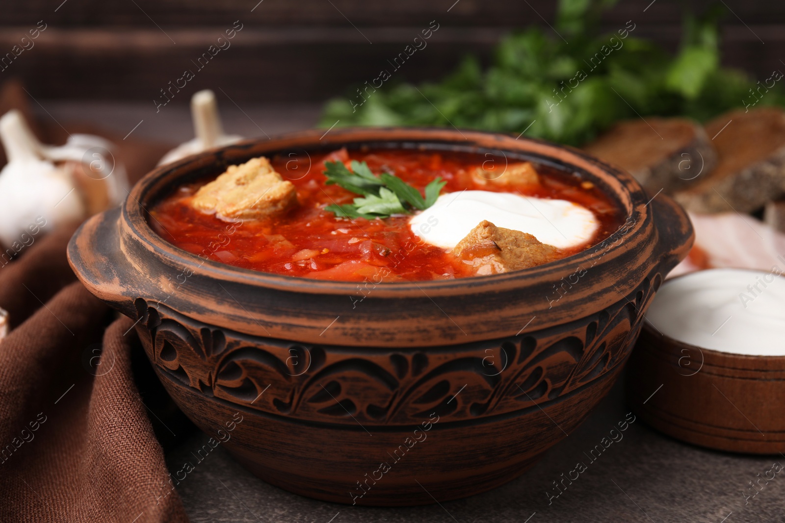 Photo of Tasty borscht with sour cream in bowl on brown textured table, closeup