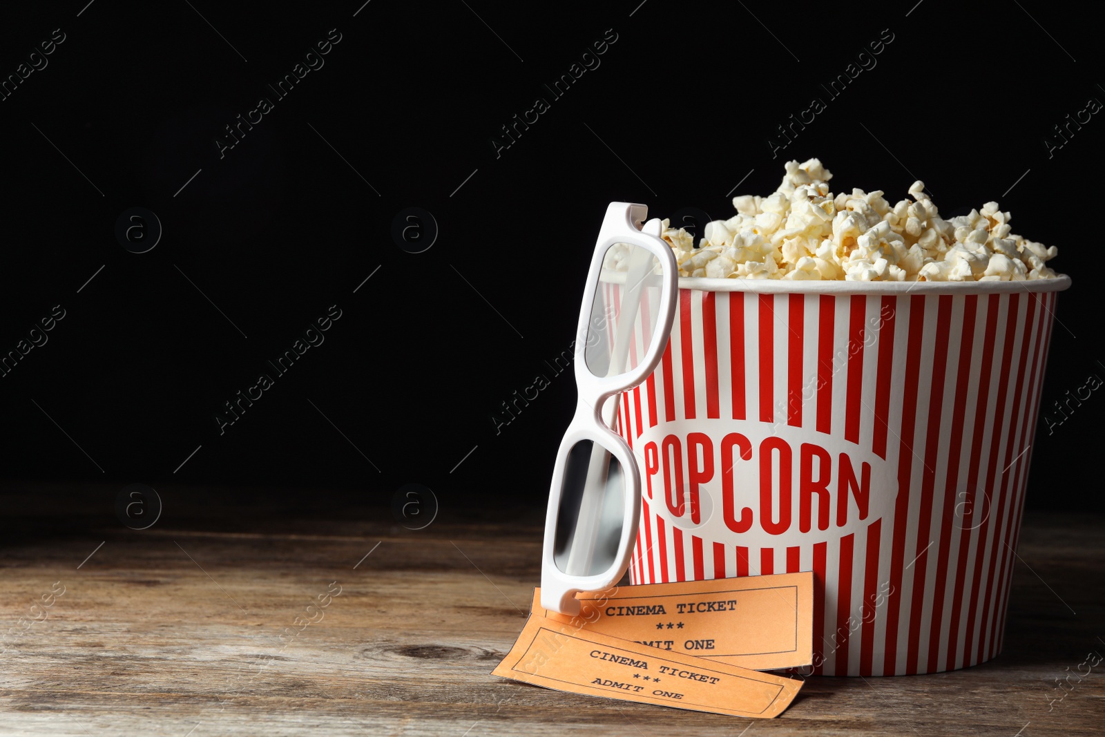 Photo of Popcorn, cinema tickets and 3d glasses on wooden table against black background. Space for text