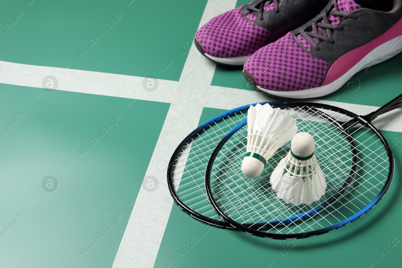 Photo of Feather badminton shuttlecocks, rackets and sneakers on court, space for text