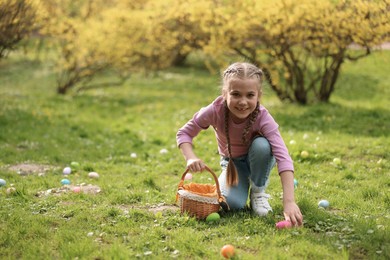 Easter celebration. Cute little girl hunting eggs outdoors, space for text