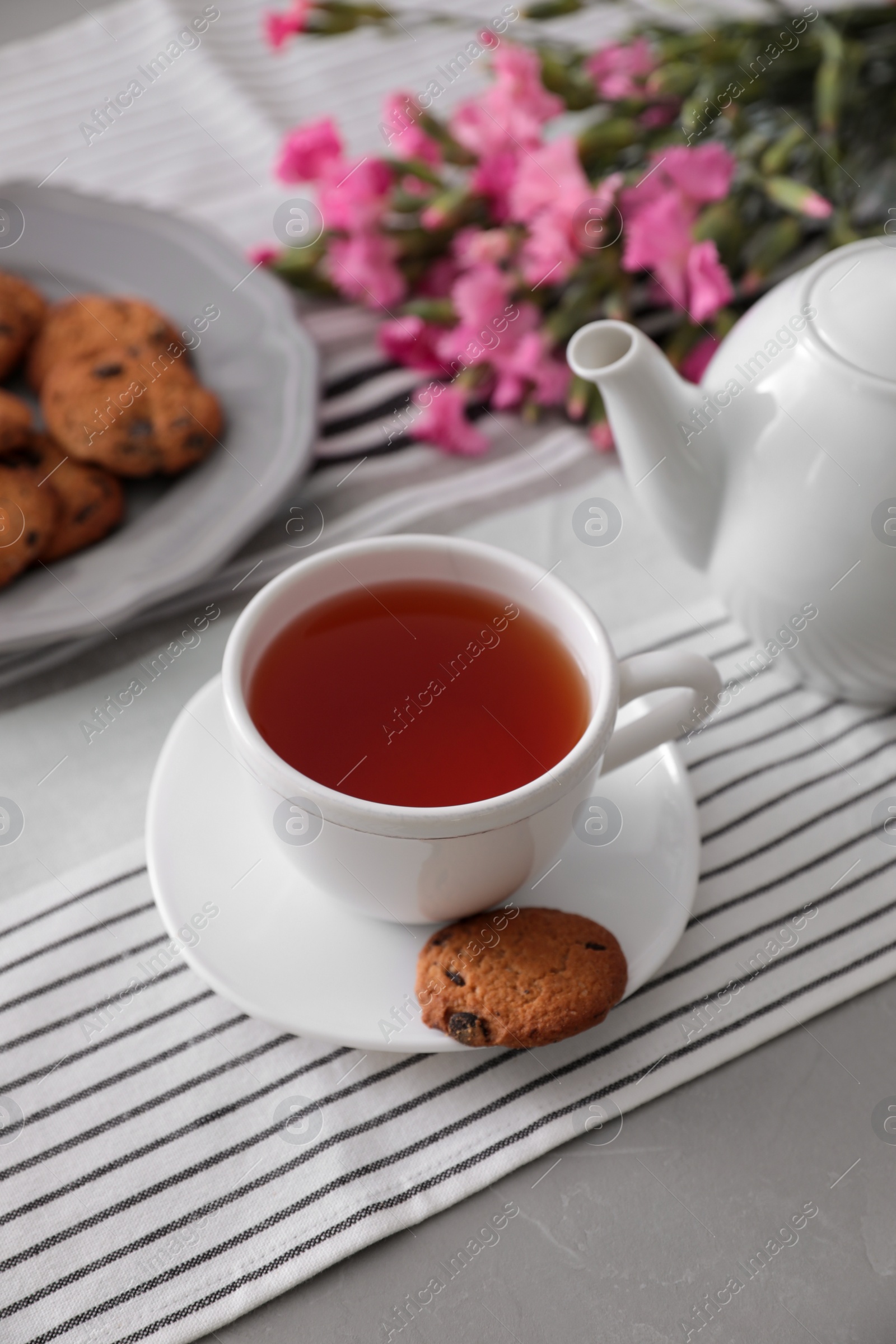 Photo of Cup of aromatic tea and tasty cookies on grey table