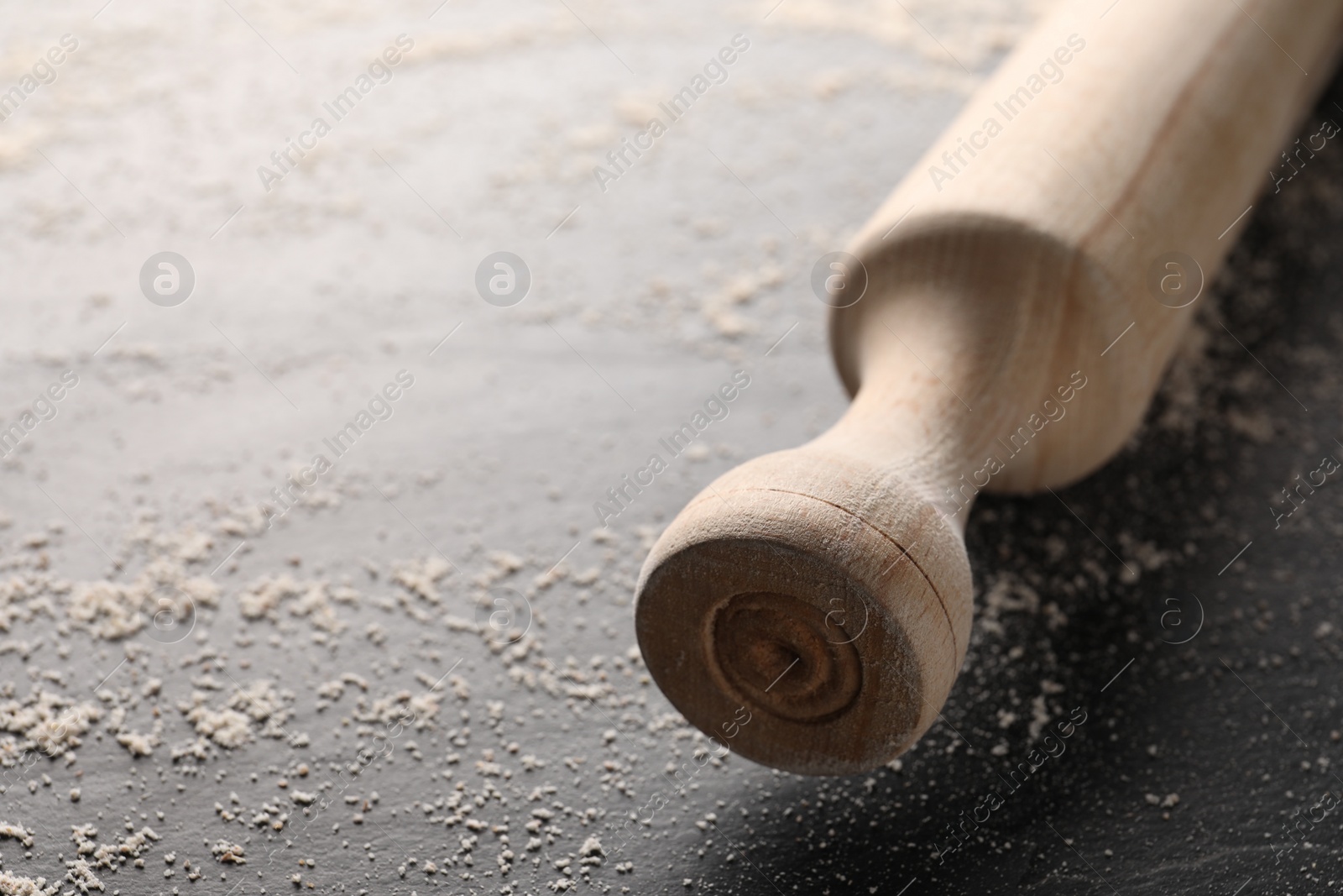 Photo of Scattered flour and rolling pin on dark textured table, closeup. Space for text