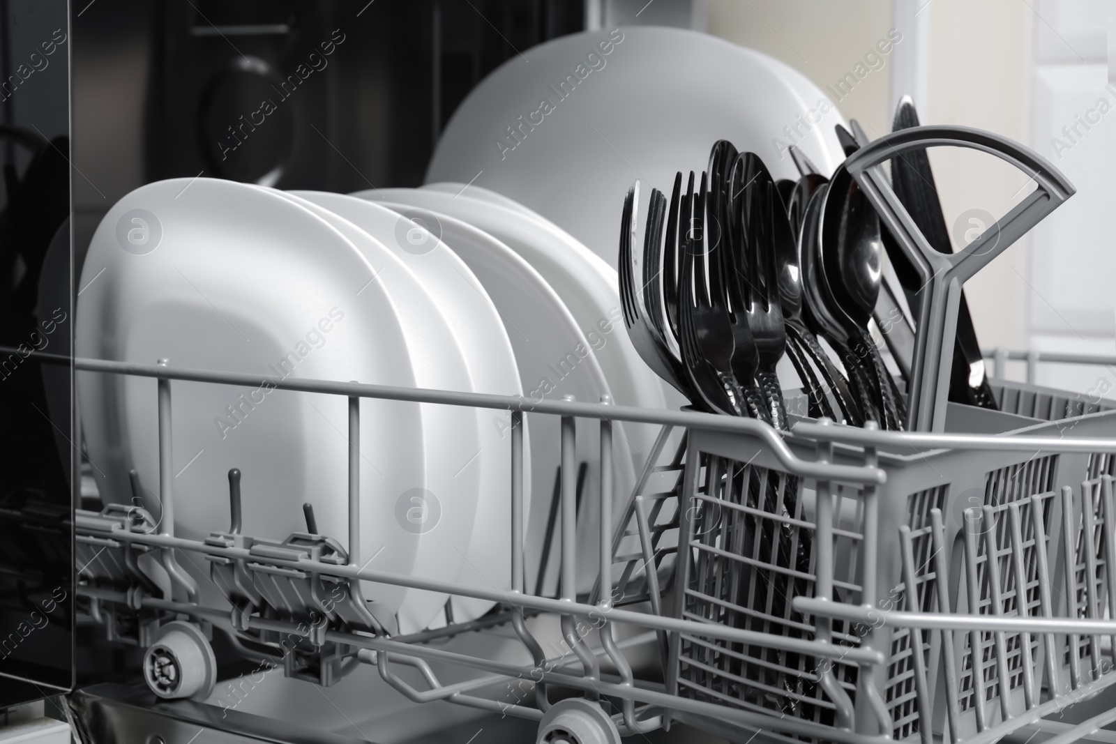 Photo of Open modern dishwasher with clean tableware, closeup