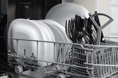 Open modern dishwasher with clean tableware, closeup