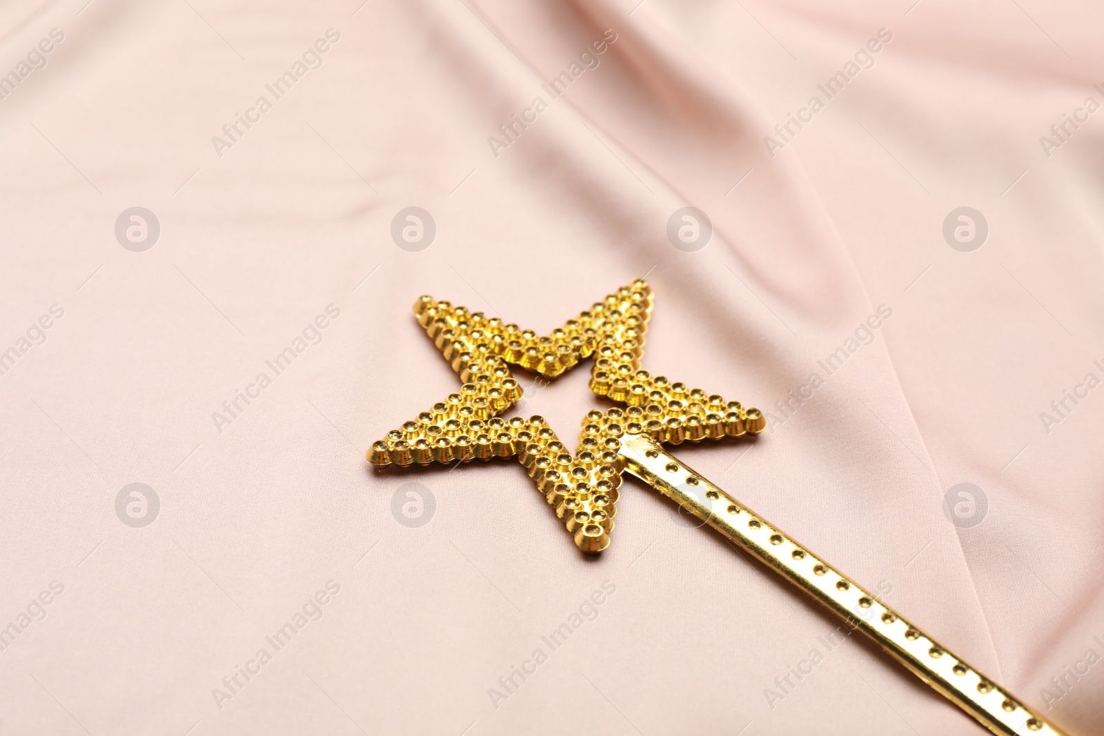 Photo of Beautiful golden magic wand on pink fabric