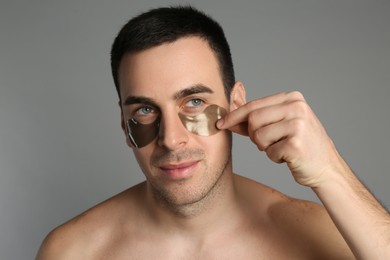 Young man applying under eye patches on grey background