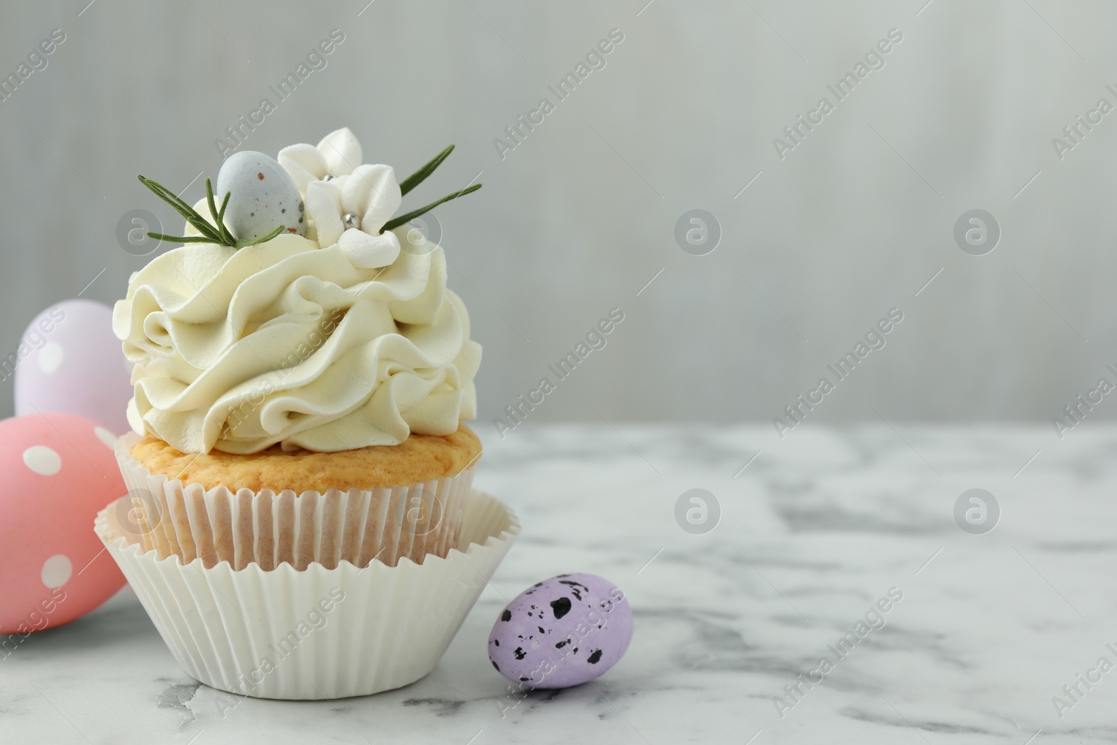 Photo of Tasty Easter cupcake with vanilla cream and eggs on white marble table, space for text