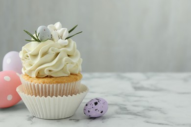 Photo of Tasty Easter cupcake with vanilla cream and eggs on white marble table, space for text