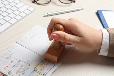 Ukraine, Lviv - September 6, 2022: Woman stamping visa page in passport at white wooden table, closeup