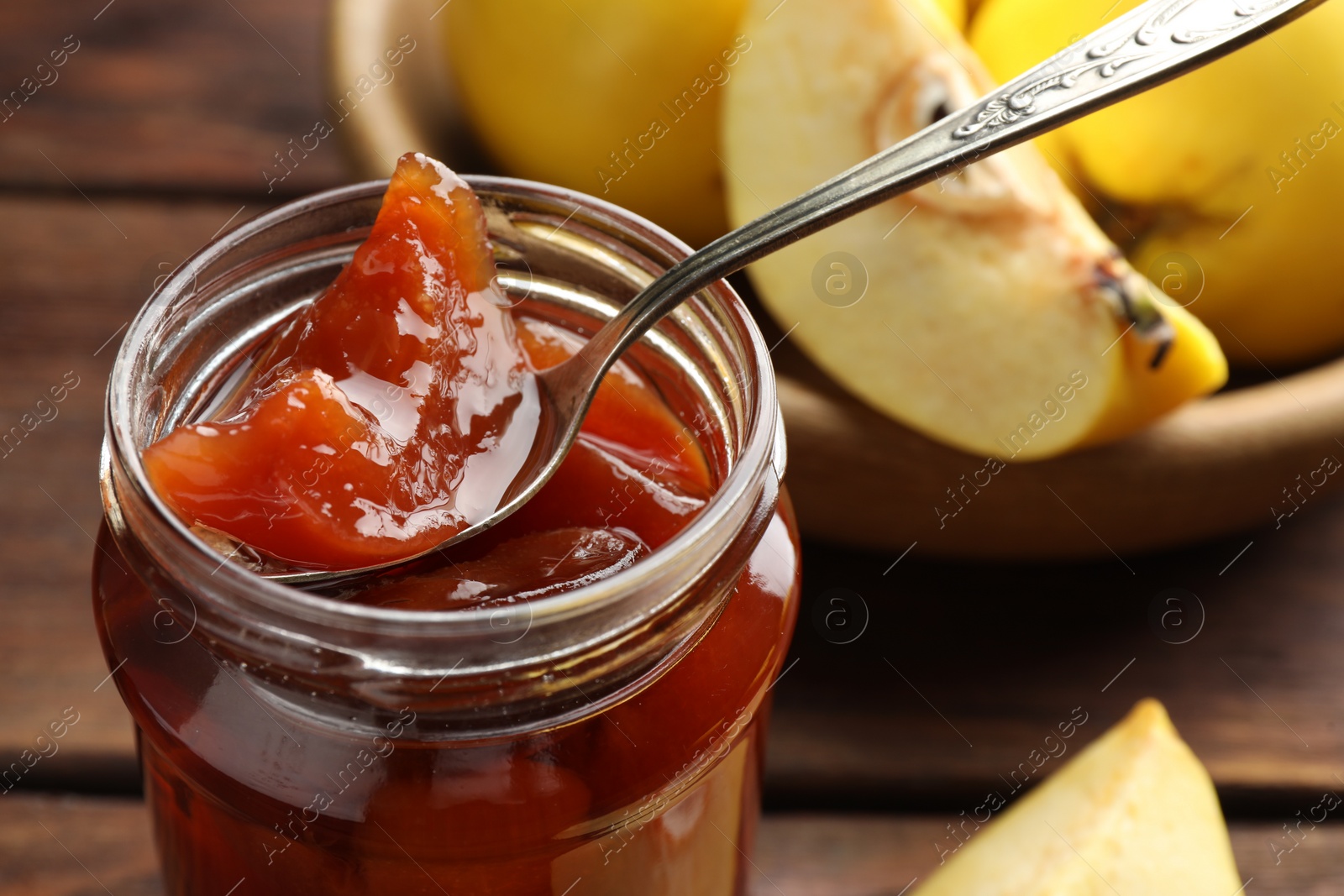 Photo of Taking tasty homemade quince jam from jar at table, closeup