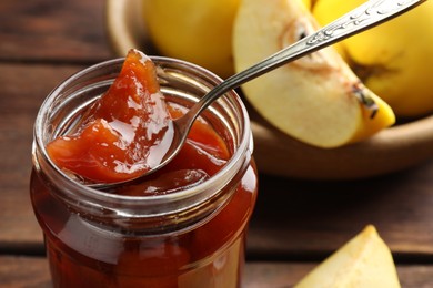 Photo of Taking tasty homemade quince jam from jar at table, closeup