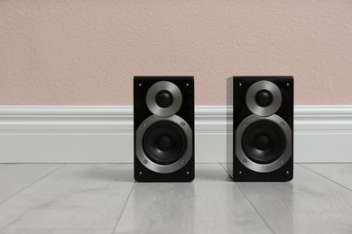 Photo of Modern powerful audio speakers on floor near pink wall