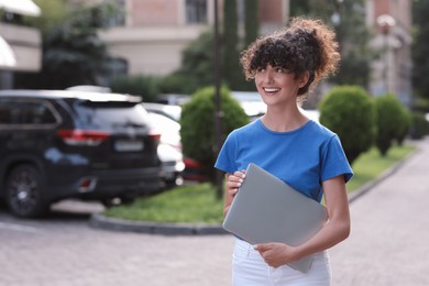 Photo of Happy young woman holding modern laptop on city street. Space for text